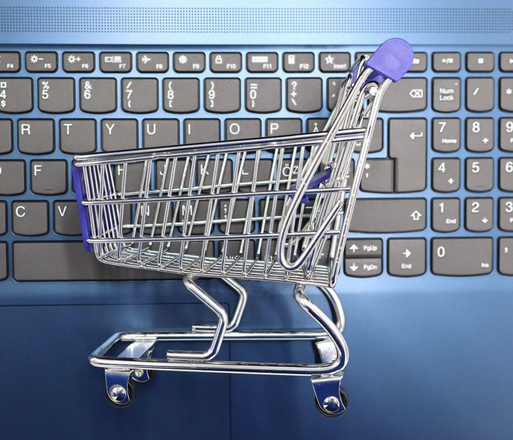 Mini chariot de supermarché métallique posé sur le clavier d'un ordinateur portable, symbole de l'achat en ligne