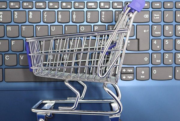 Mini chariot de supermarché métallique posé sur le clavier d'un ordinateur portable, symbole de l'achat en ligne