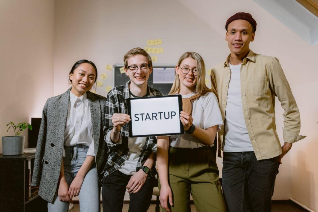 Une équipe de jeune startup souriante tenant une tablette affichant le mot STARTUP dans un bureau
