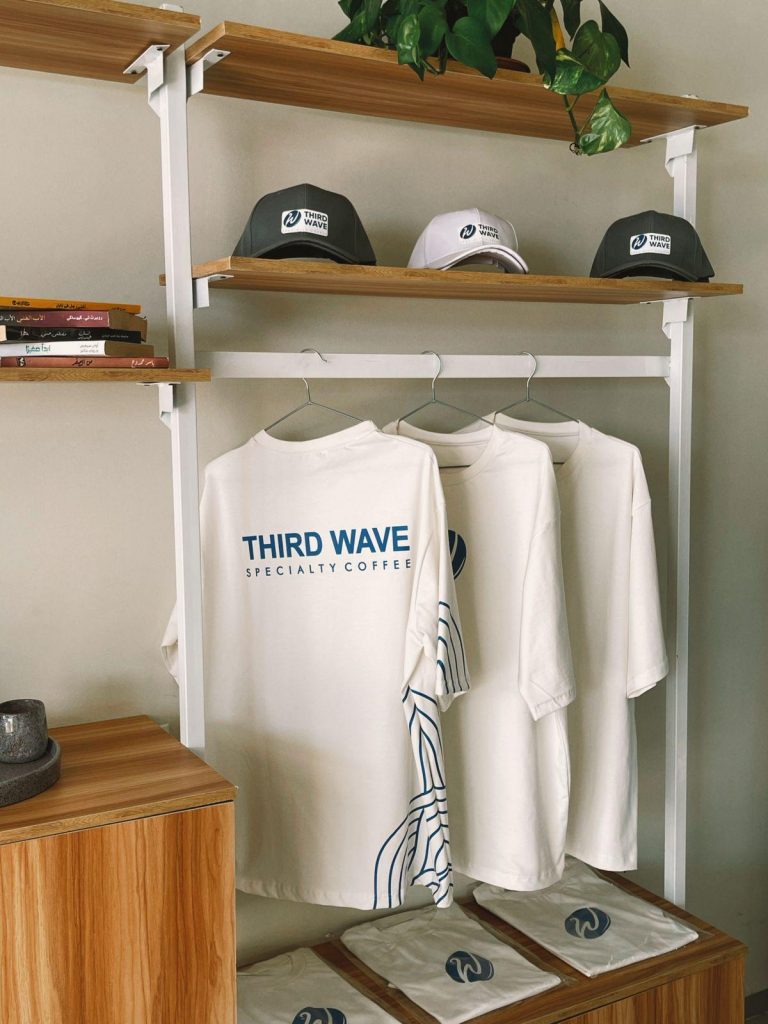 Rangée de t-shirts blancs floqués et de casquettes brodées d'un logo de marque suspendus sur des cintres